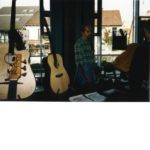 1997 Wieslocher Gitarrentage: Christian Stoll presents his instruments. Left in the foreground two Legendary Acoustic Basses of the third generation. Right in the foreground flyer for the first time offered guitar building workshops